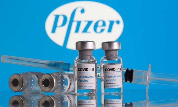 Frascos rotulados como de vacina contra Covid-19 em frente ao logo da Pfizer